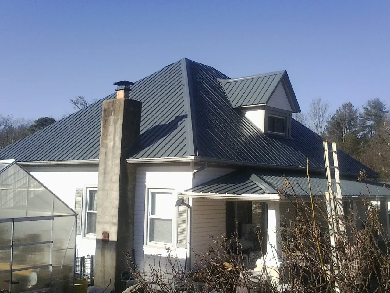Dark blue standing seam metal roof on a white farmhouse with dormer — Slate & Tile Roof Repair by Roofing Brothers in Saltsburg