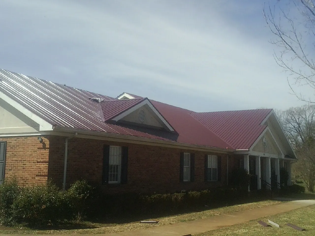 Red metal roof with gabled entries on a long brick building, from a Hail Damage Roof Repair job in Saltsburg