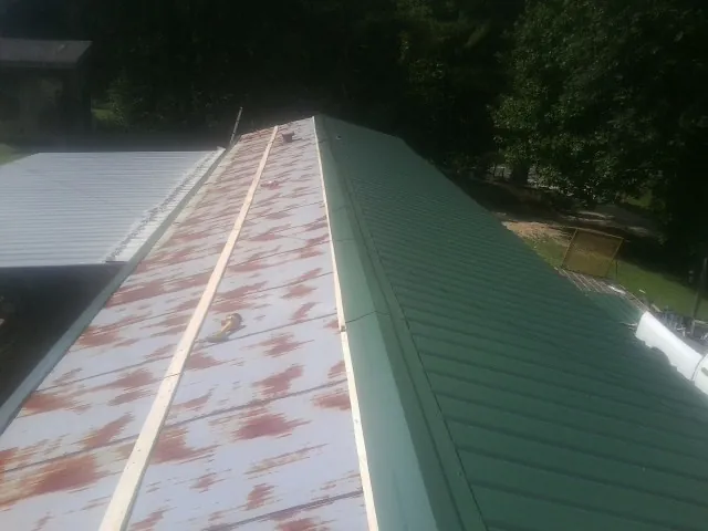 Old rusted panels beside newly installed green metal roofing — Wind Damage Roof Repair by Roofing Brothers in Saltsburg