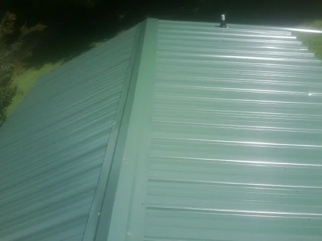 New green metal panels meeting at the ridge of a roof — Flat Roof Repair work by our crew in Saltsburg