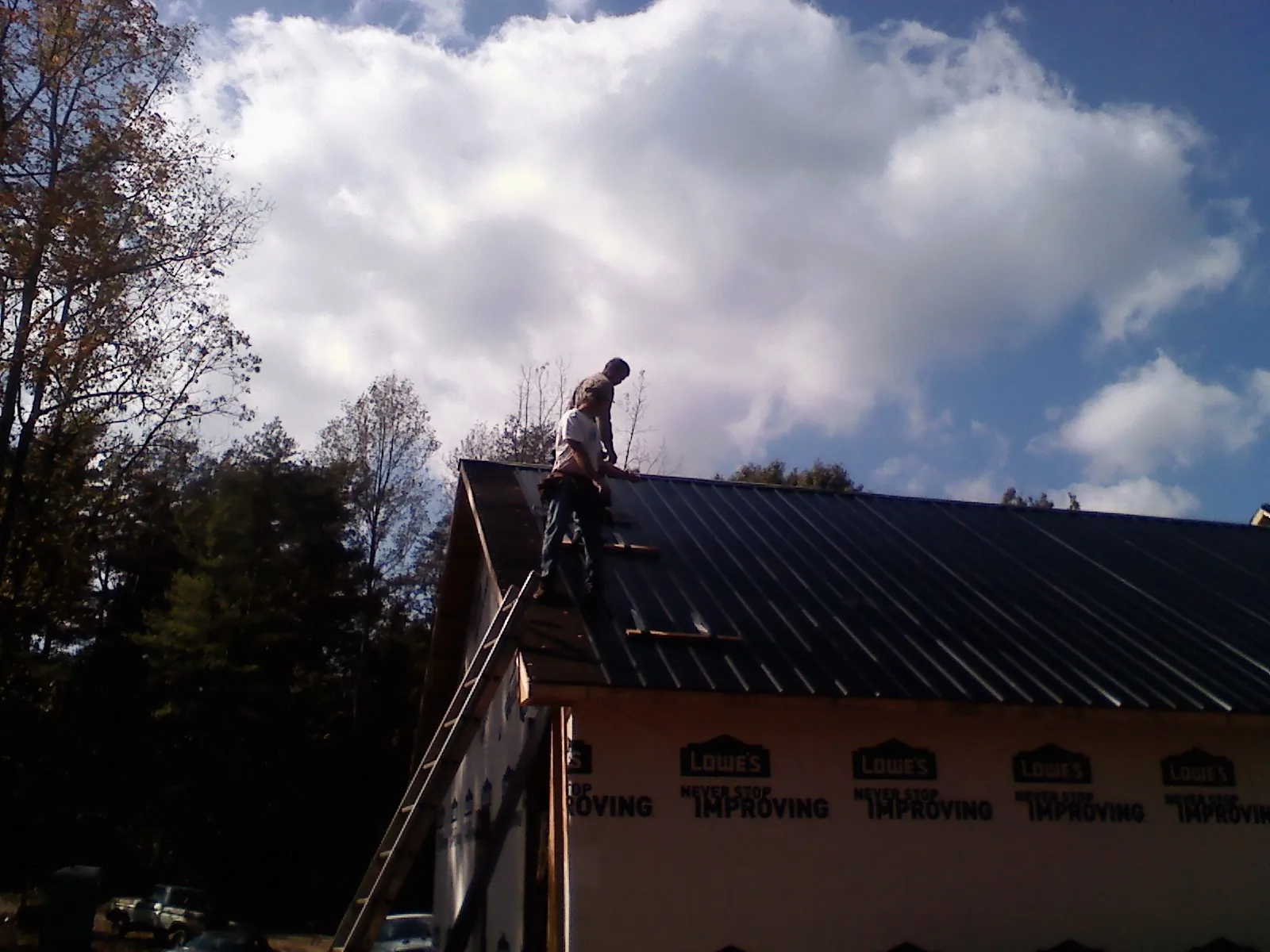 Roofer fastening dark metal panels high against a cloudy sky, from a Roof Inspection job in Saltsburg
