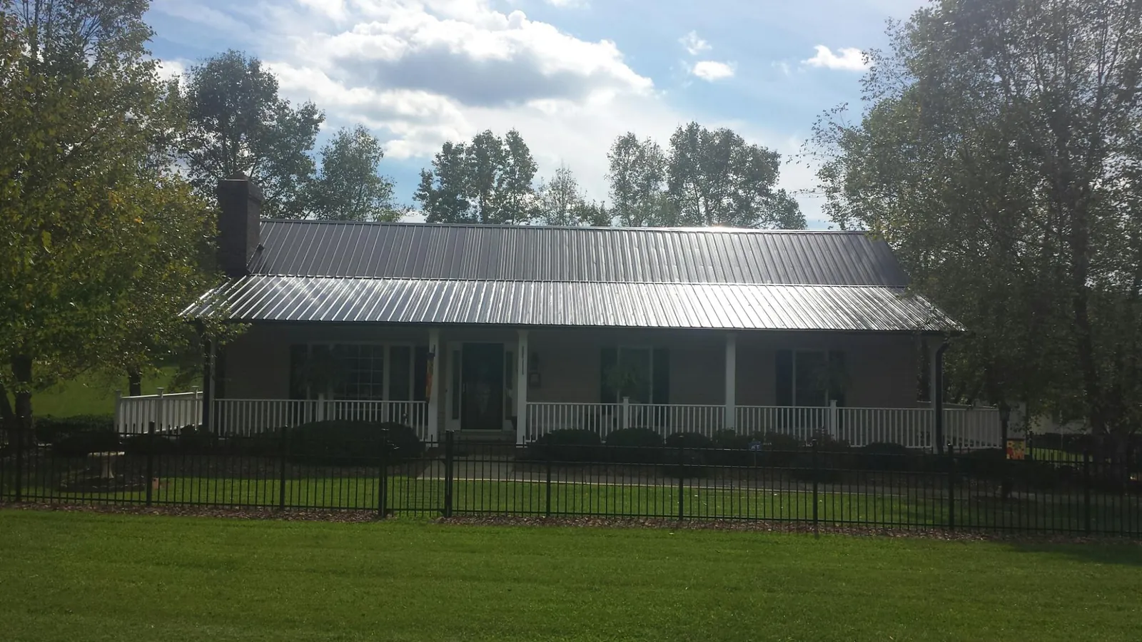 Gray metal roof on a brick ranch with a full width front porch — Gutter Guard Installation work by our crew in Saltsburg