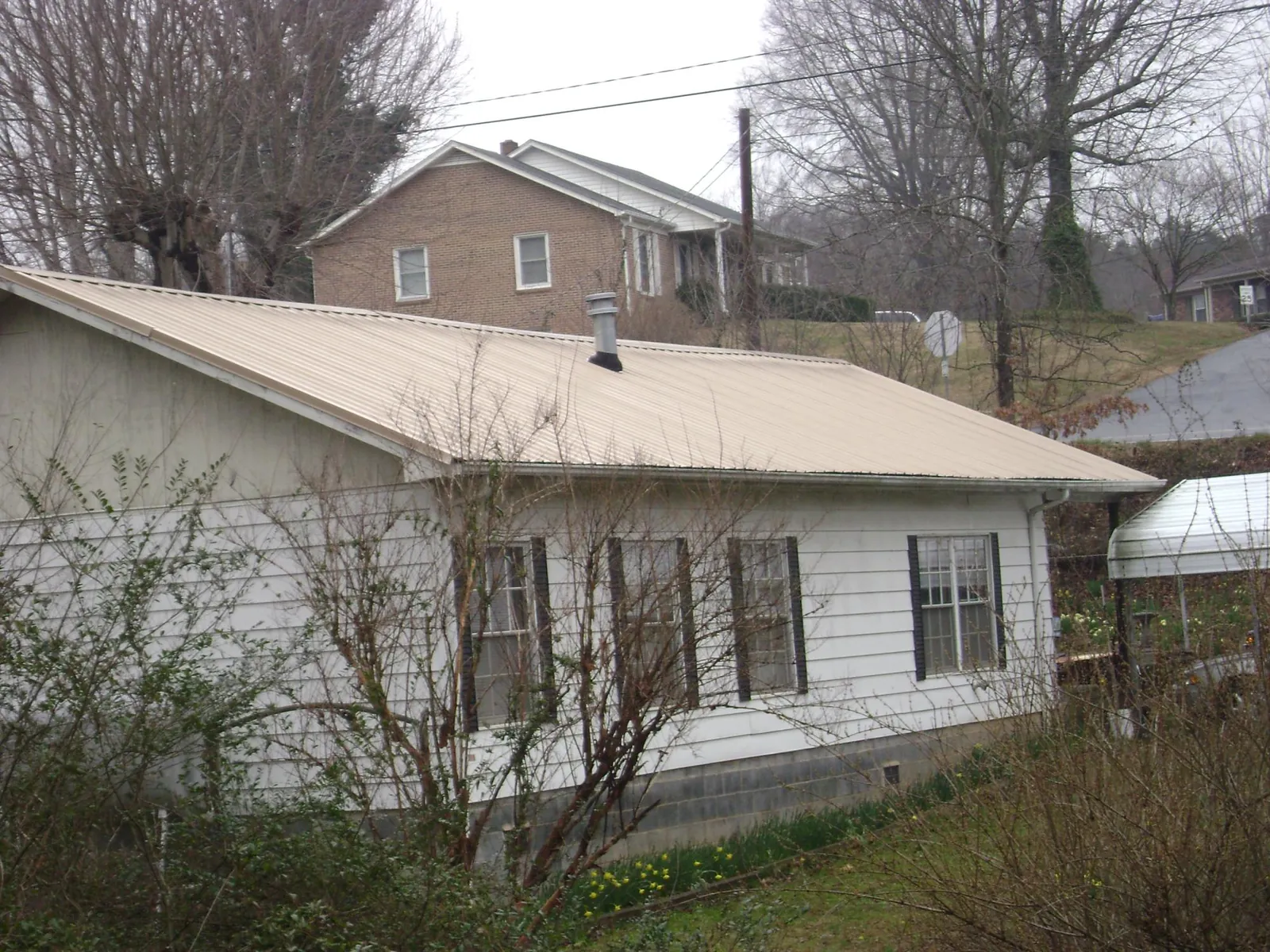 Tan metal roof on a white sided house set into a hillside — Commercial Roofing by Roofing Brothers in Saltsburg