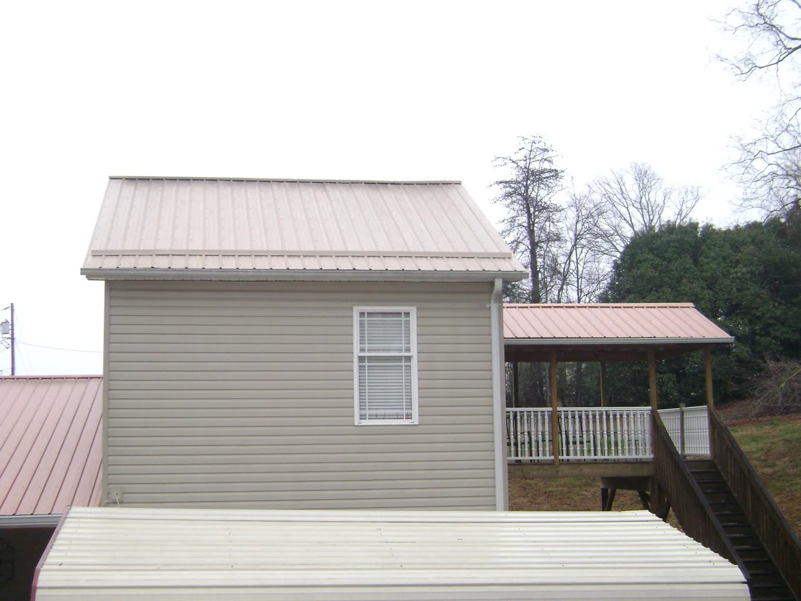 Tan metal roofs on a two story addition and attached porch, from a Roof Replacement job in Saltsburg